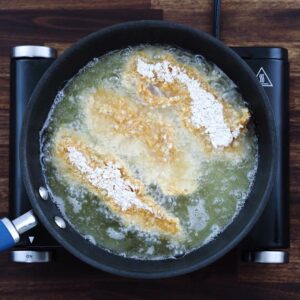 Breaded chicken tenders frying in oil.