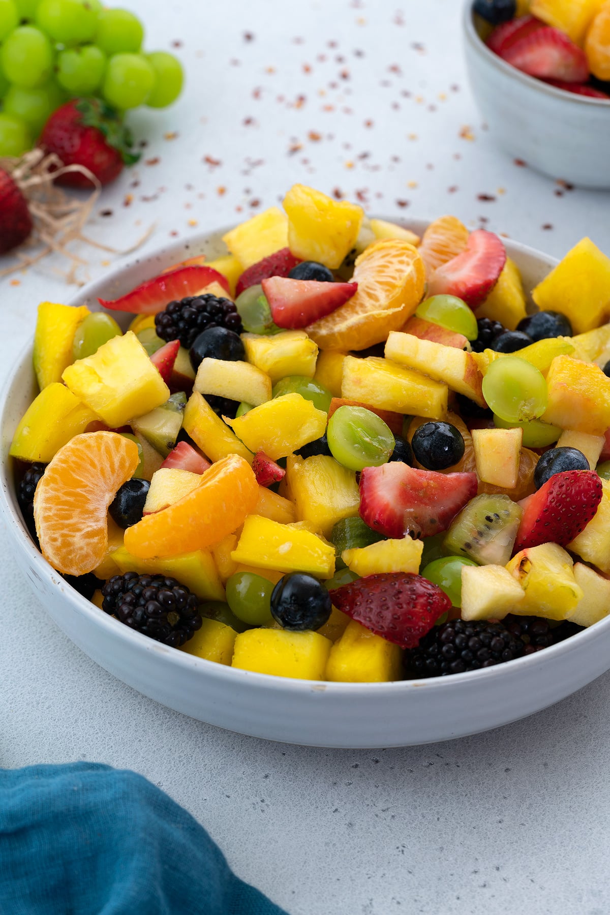 Homemade fruit salad with a variety of fruits in a white bowl placed on a clean white table.
