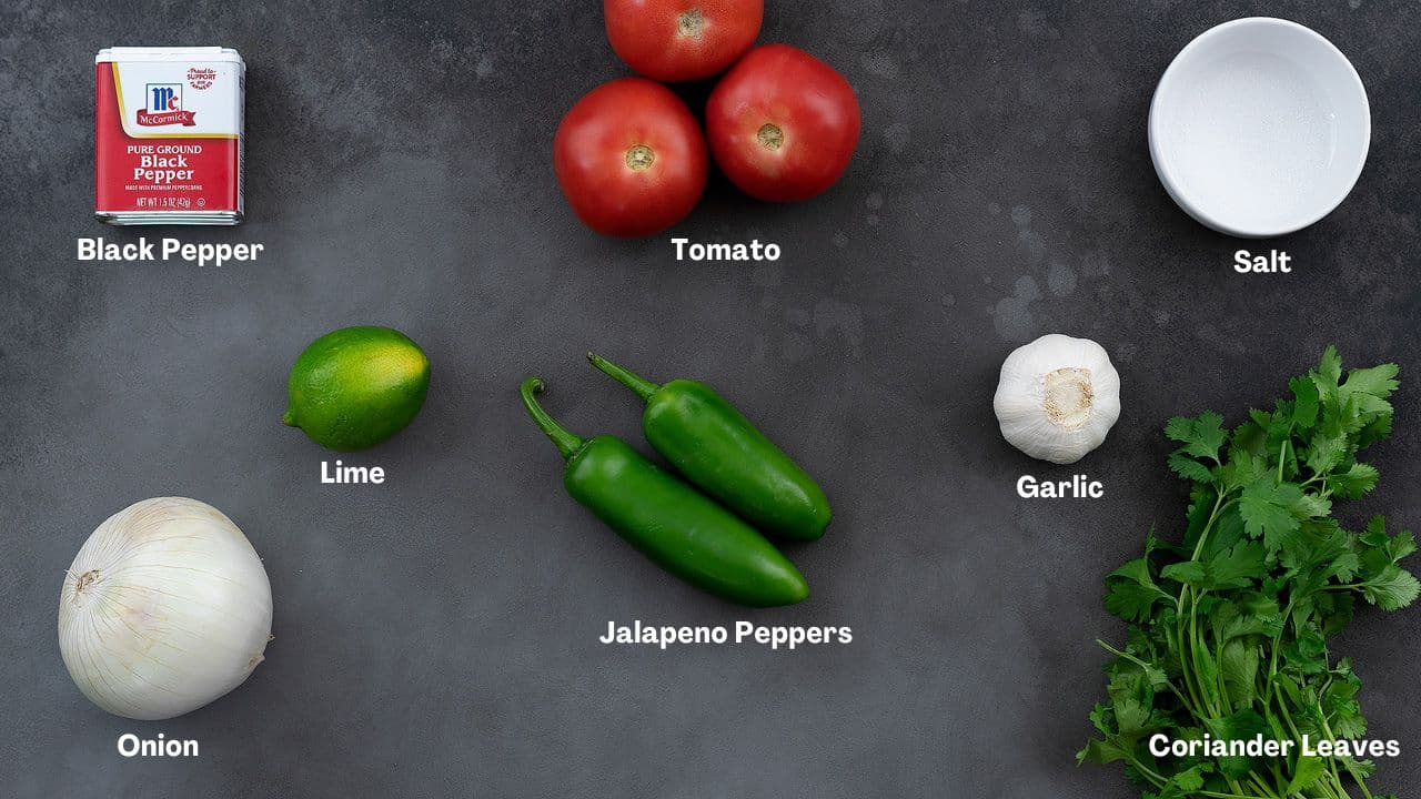 Pico de gallo recipe Ingredients such as tomatoes, onion, jalapeno, lime, and cilantro on a grey table.