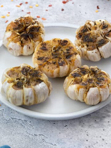 Roasted Garlic heads arranged on a white plate and few ingredients scattered around.