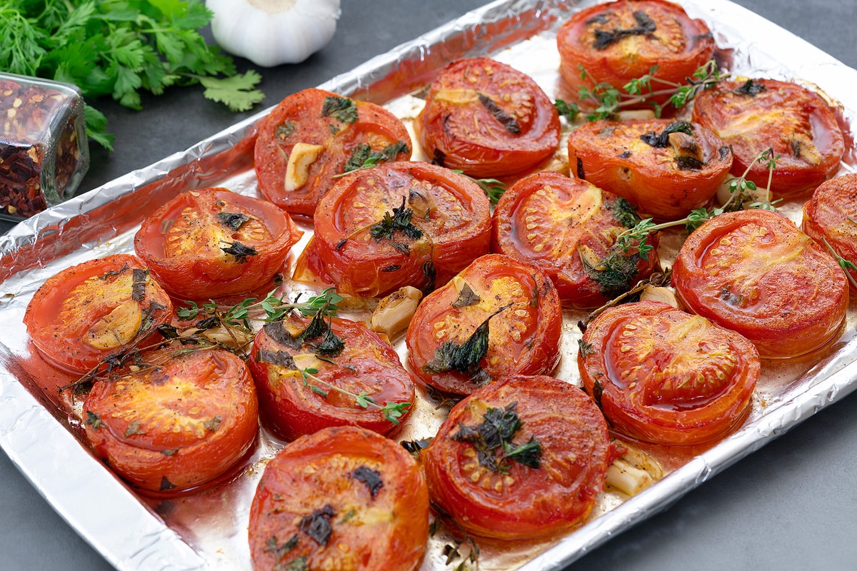 Oven Roasted Tomatoes in a baking tray with few ingredients arranged around.