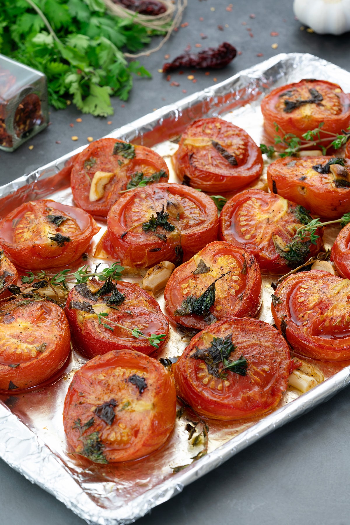 Oven Roasted Tomatoes in a baking tray with few ingredients scattered around.
