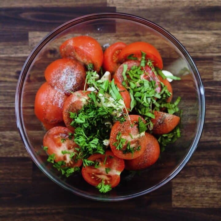 A bowl with halved tomatoes and seasoning.