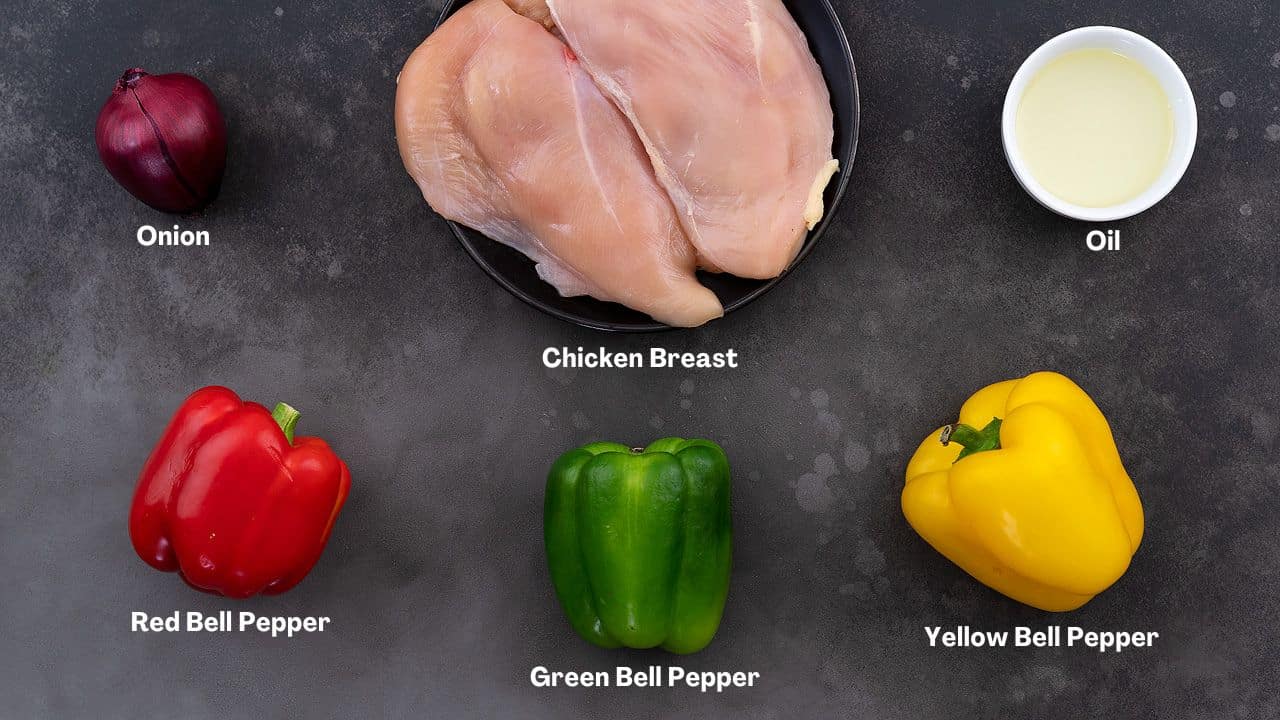 Assorted Chicken Fajita Ingredients neatly arranged on a grey table. Featuring tender chicken breasts, vibrant red, green, and yellow bell peppers, onions, and a bottle of oil.