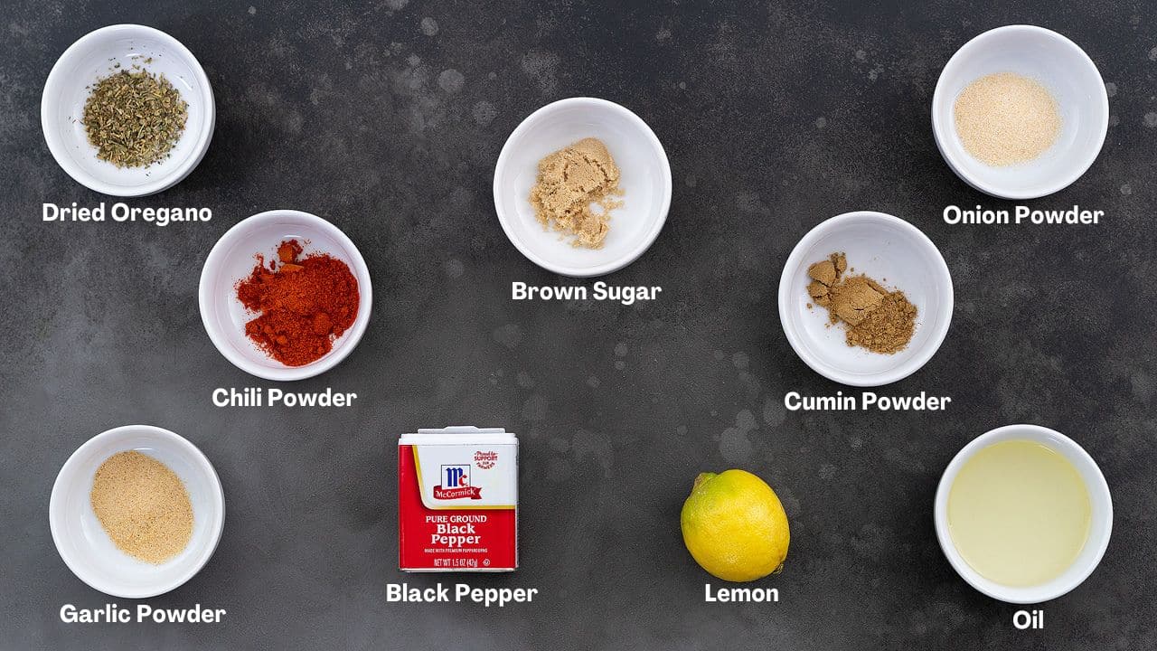 Chicken Fajita recipe ingredients on a grey table, including Dried Oregano, Brown Sugar, Onion Powder, Chili Powder, Cumin Powder, Garlic Powder, Black Pepper, Lemon, and Oil.