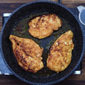 Chicken breast frying in a pan.