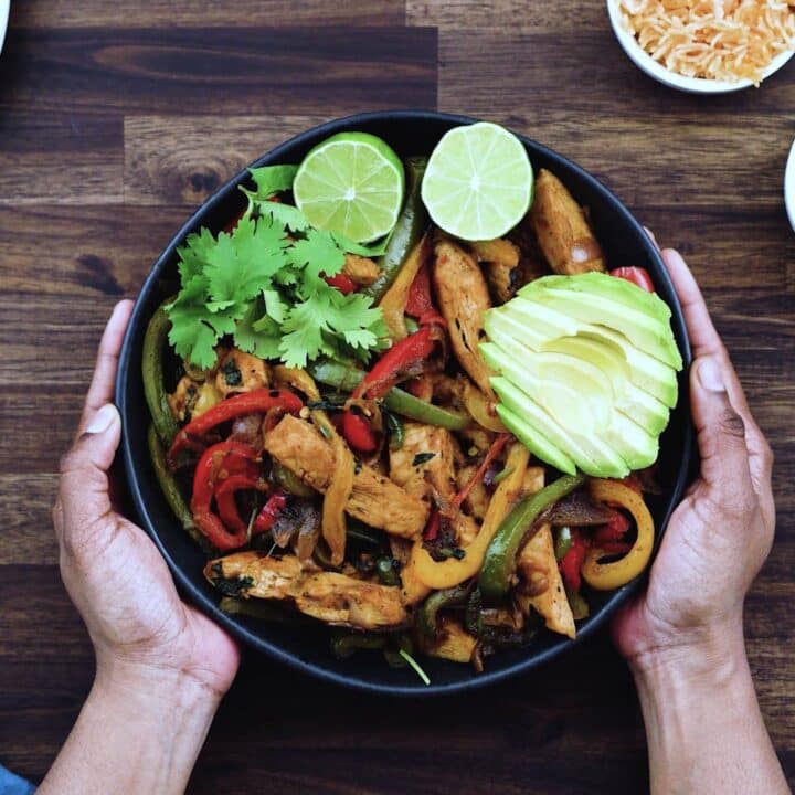 Serving chicken fajitas topped with avocado and lime slices in a black bowl.