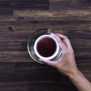 Adding red wine vinegar to make Greek salad dressing to a bowl.