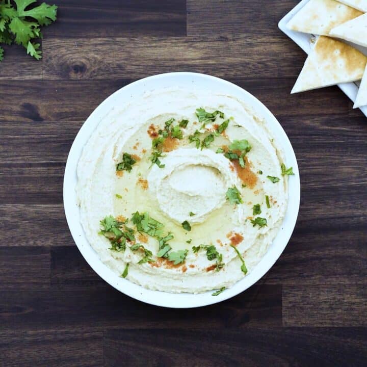Hummus served in white bowl with pita bread alongside.