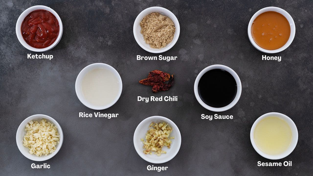 Ingredients for the sweet and spicy sauce used to coat Korean fried chicken include ketchup, brown sugar, honey, rice vinegar, soy sauce, ginger, sesame oil, and dried red chili. These ingredients are arranged in cups on a grey table.