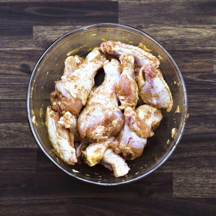 A bowl with marinated chicken wings and drumsticks.