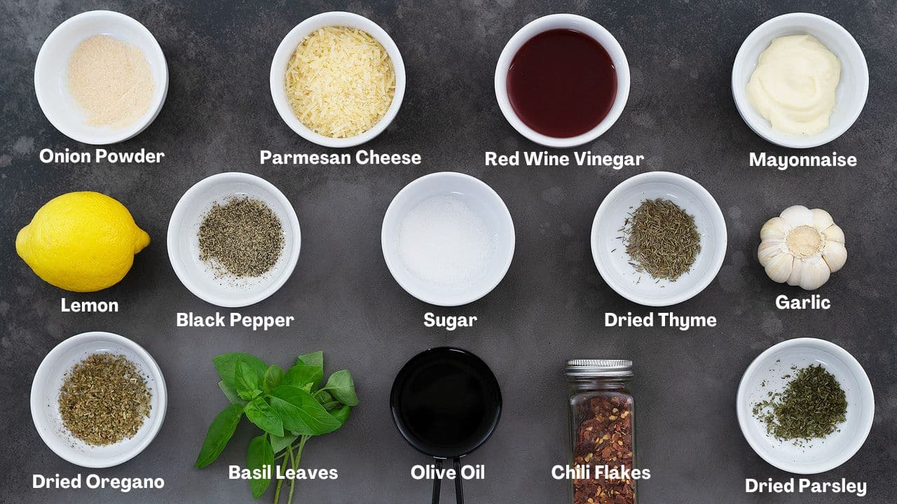 Pasta Salad dressing recipe Ingredients arranged on a grey table featuring Italian herbs, parmesan cheese, red wine vinegar, basil leaves, and more.