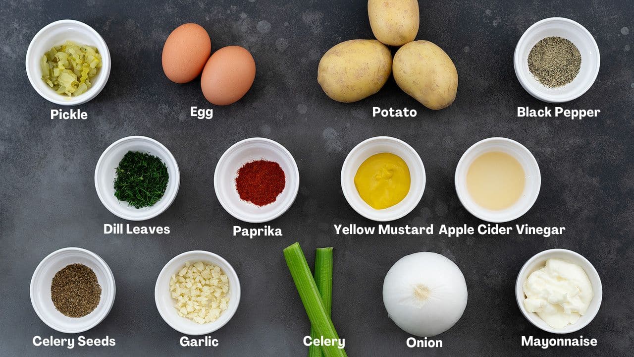 Potato salad ingredients on a gray table. The ingredients include pickles, eggs, potatoes, black pepper powder, dill leaves, paprika, yellow mustard, apple cider vinegar, celery seeds, garlic, celery, onion, and mayonnaise.