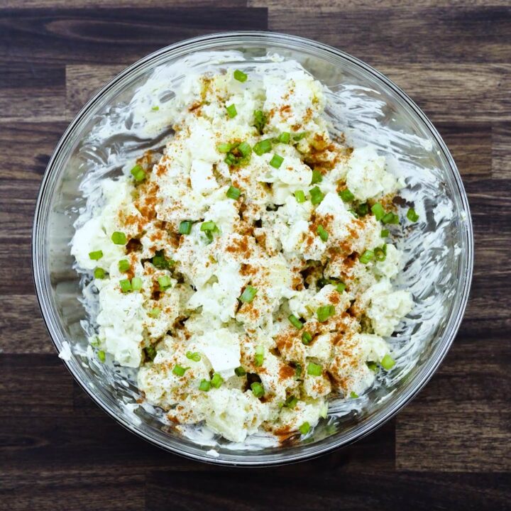 A bowl with Potato Salad garnished with paprika and spring onions.