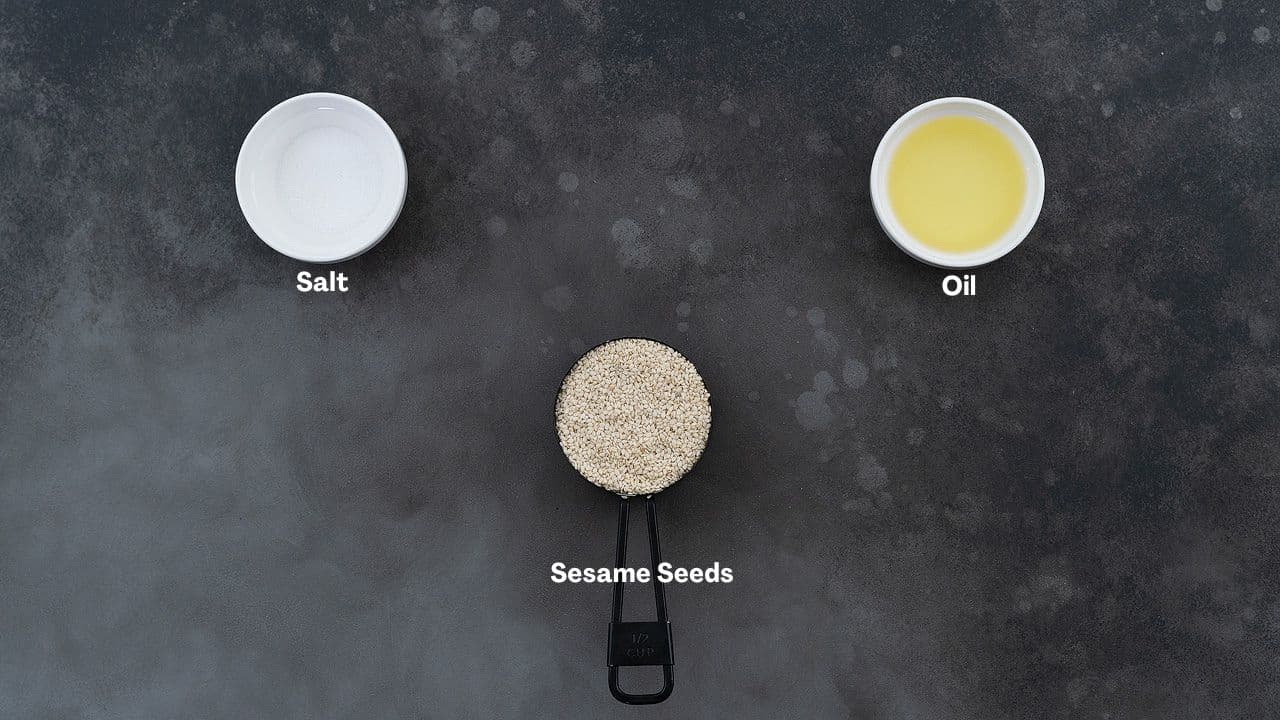 Ingredients for tahini recipe, including sesame seeds, neutral oil, and salt, arranged in black and white cups on a grey table.