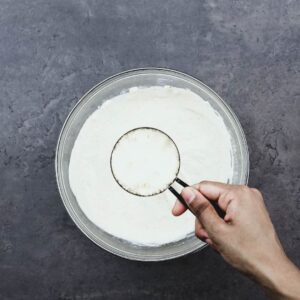 Adding Parmesan cheese to the salad dressing ingredients in bowl.