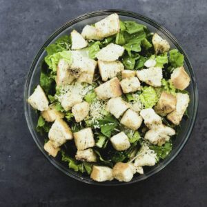 A bowl with lettuce, croutons and parmesan cheese.