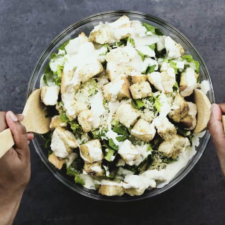 Dressing the Caesar salad with Caesar dressing using wooden spoon.