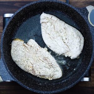 Breaded chicken breast frying in a pan.