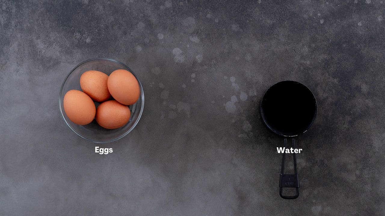 Eggs and water in a bowl and cup placed on a grey table for making soft and hard boiled eggs.
