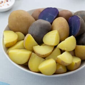 Close up of Assorted Boiled Potatoes in a White Bowl - Medley, Yukon Gold potatoes boiled whole and Honey Gold potatoes boiled and cubed, they are in purple, red and yellow colors.