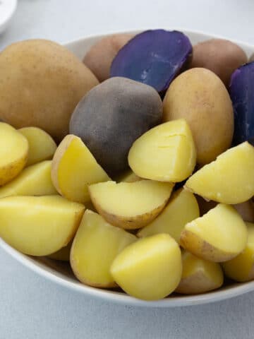 Close up of Assorted Boiled Potatoes in a White Bowl - Medley, Yukon Gold potatoes boiled whole and Honey Gold potatoes boiled and cubed, they are in purple, red and yellow colors.
