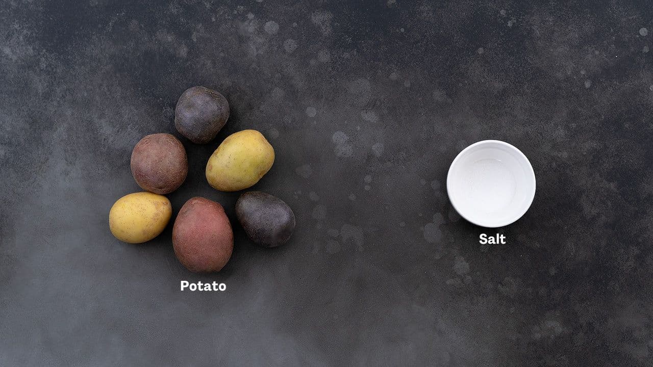 Colorful Assorted Boiled Potato Recipe Ingredients - A medley of purple, red, and yellow Yukon Gold potatoes arranged on a grey table along with a small bowl of salt.