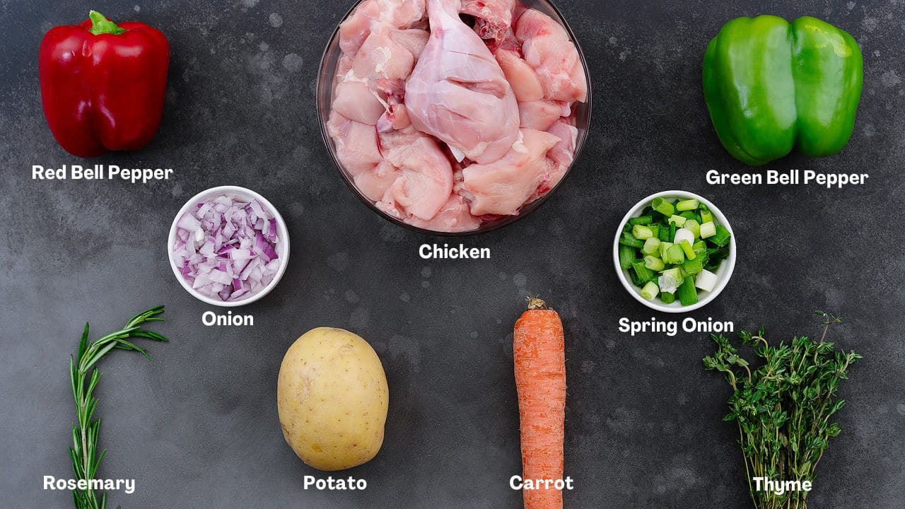 Ingredients for Jamaican curry chicken arranged on a grey table. The ingredients include vibrant red bell peppers, succulent chicken pieces, onions, spring onions, sprigs of rosemary, hearty potatoes, carrots, and thyme leaves.