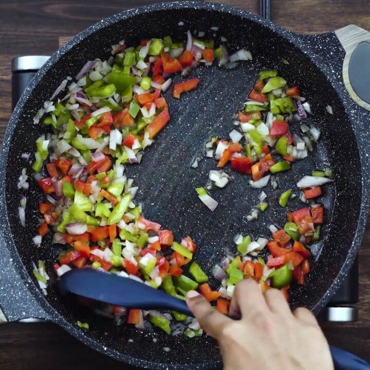 Sauteing onions and bell peppers in a pan.