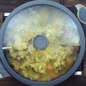 A pan with chicken and veggies cooking with lid closed.