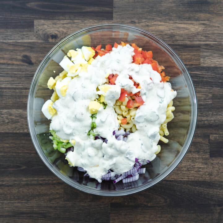 A bowl with Macaroni Salad ingredients topped with dressing.