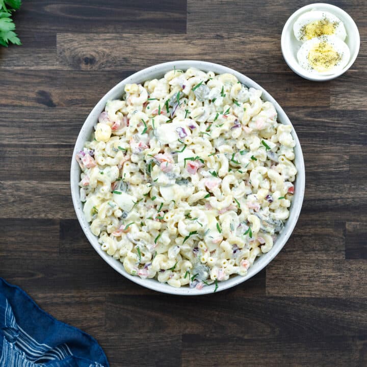 Macaroni Salad served in a white bowl with boiled egg nearby.