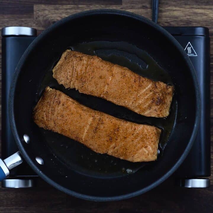 Salmon fillets frying in a pan.