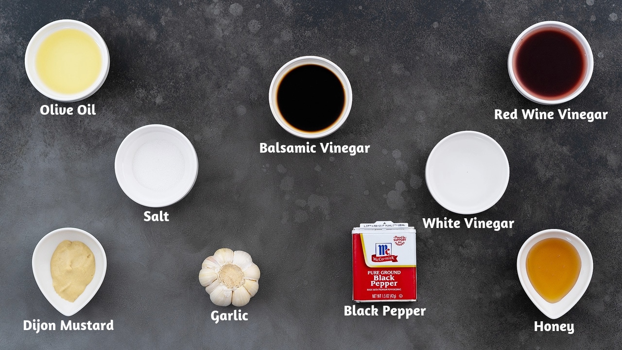 Three rows of vinaigrette ingredients arranged on a grey table. The first row contains olive oil, balsamic vinegar, and red wine vinegar. The second row contains salt and white vinegar. The third row contains Dijon mustard, garlic, black pepper, and honey.