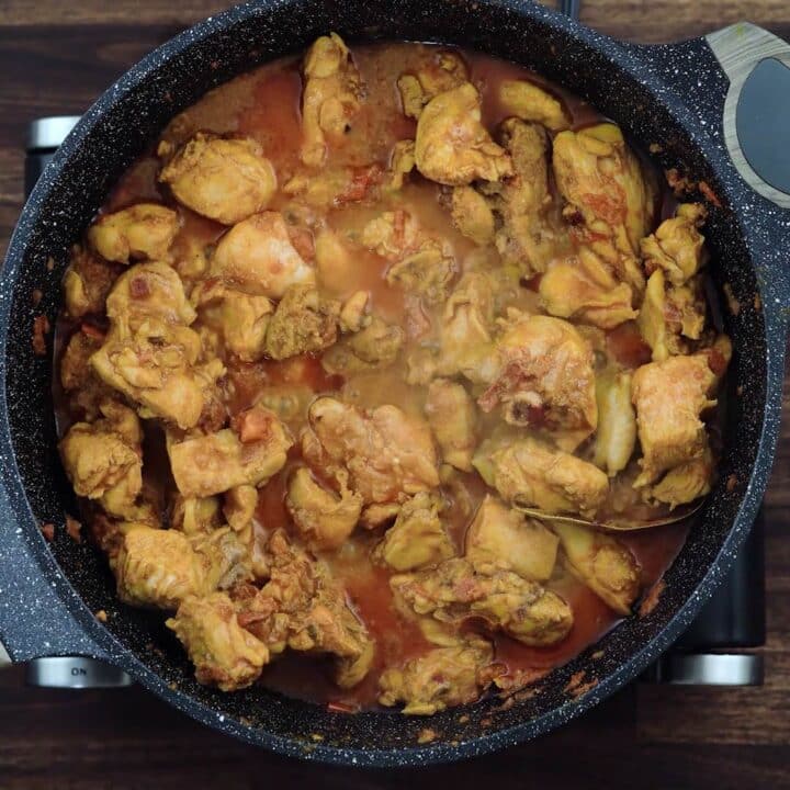 A pan with marinated chicken in onion tomato masala.