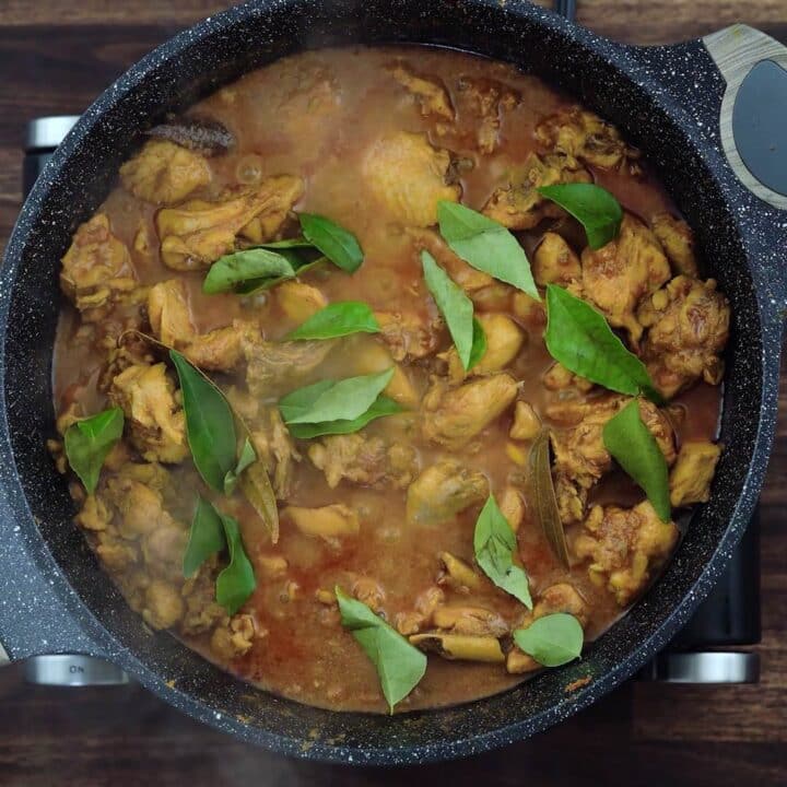 A pan with chicken masala garnished with curry leaves.