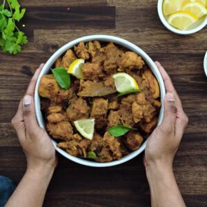 Serving Chicken Masala in white bowl topped with lemon wedges.