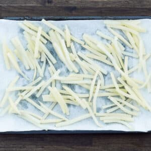 Freshly fried French fries cooling on a tray lined with paper towels.