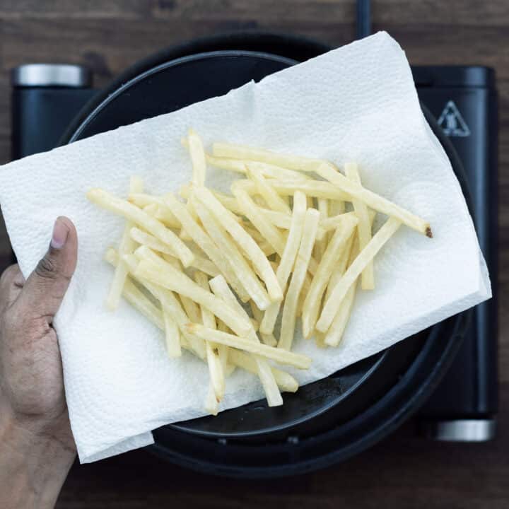Showing the crispy golden French Fries on a black plate lined with a paper towel.