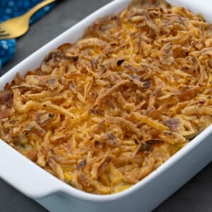 Homemade Green Bean Casserole in a white baking dish on a grey table with a blue towel, and a golden spoon nearby.