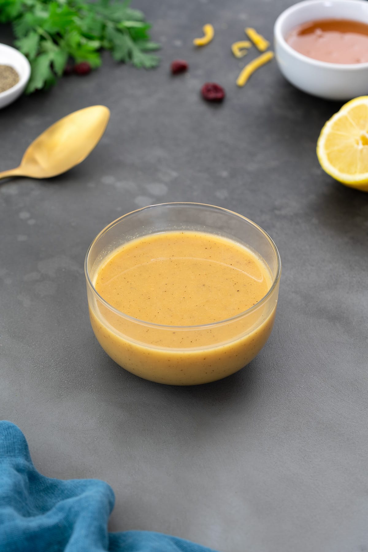 Honey mustard dressing in a glass bowl on a gray table with a cup of honey, lemon slice, and greens arranged around it.