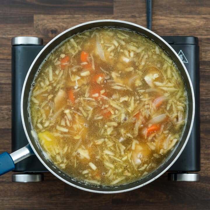 A pan with chicken and veggies immersed in chicken broth mixture alone with grated apples and other seasonings.