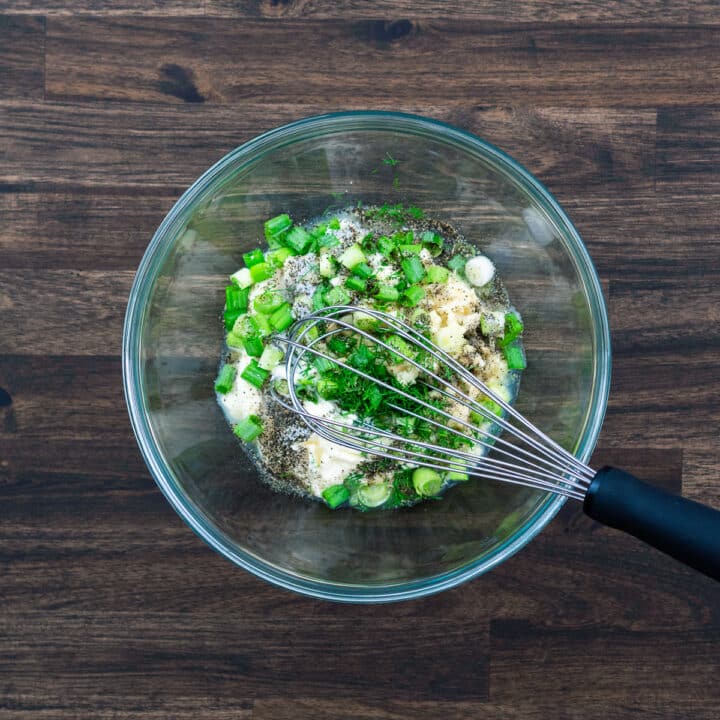 A bowl with creamy dressing ingredients and a whisker.