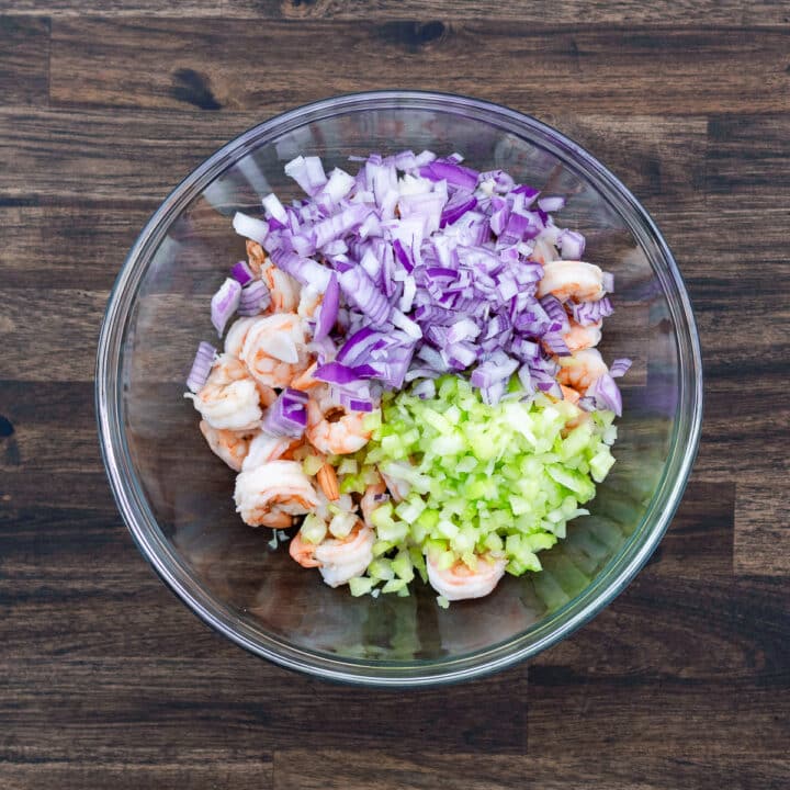 A bowl with cooked shrimp, chopped onion and celery.