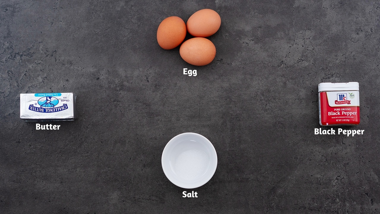 Sunny side up recipe ingredients such as egg, butter, salt, and pepper are placed on a grey table.