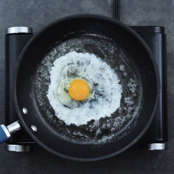 Partially cooked white of a sunny-side-up egg in a pan.