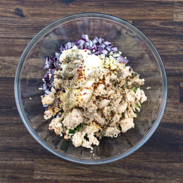 A bowl with tuna salad ingredients and seasonings like mayo, dijon and other seasonings.