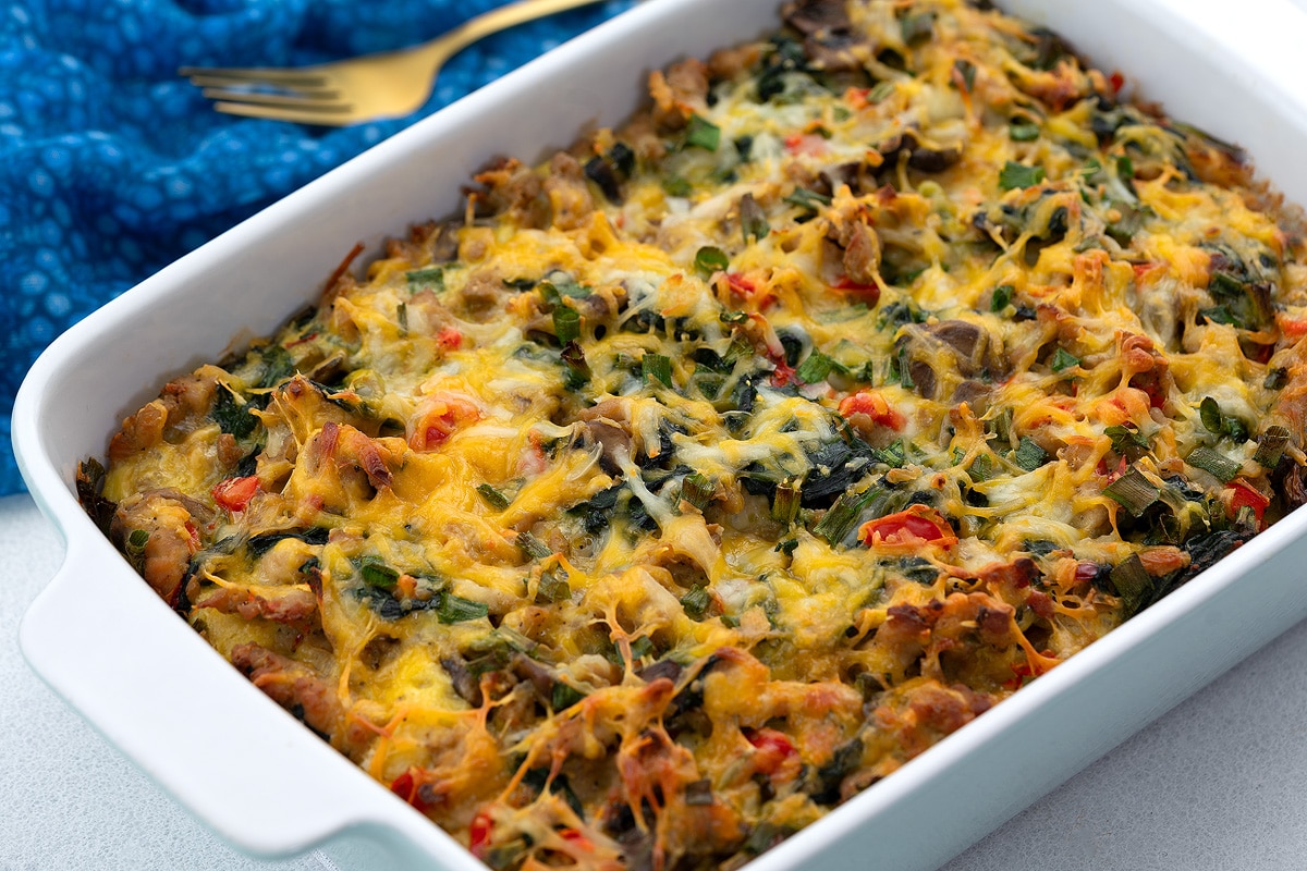 Homemade breakfast casserole in a white baking dish on a white table top with a blue towel and a golden fork.