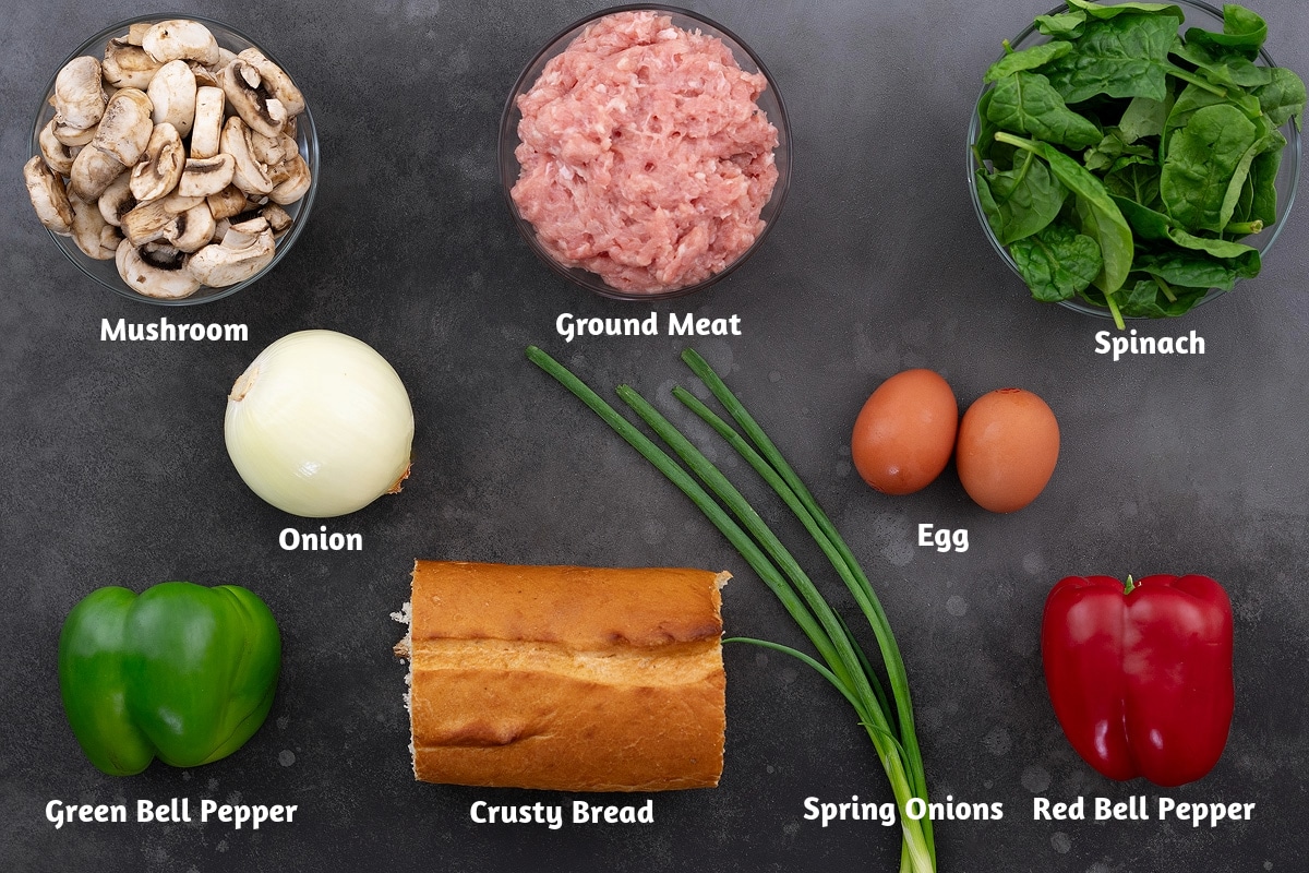 Assorted ingredients for a breakfast casserole, including mushrooms, ground meat, spinach, onion, spring onions, eggs, green bell pepper, crusty bread, and red bell pepper.