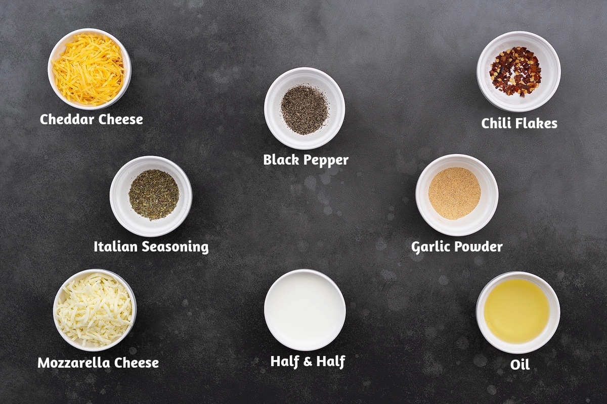 Dairy and spice ingredients for a breakfast casserole, including cheddar cheese, black pepper powder, chili flakes, Italian seasoning, garlic powder, mozzarella cheese, half and half, and oil.
